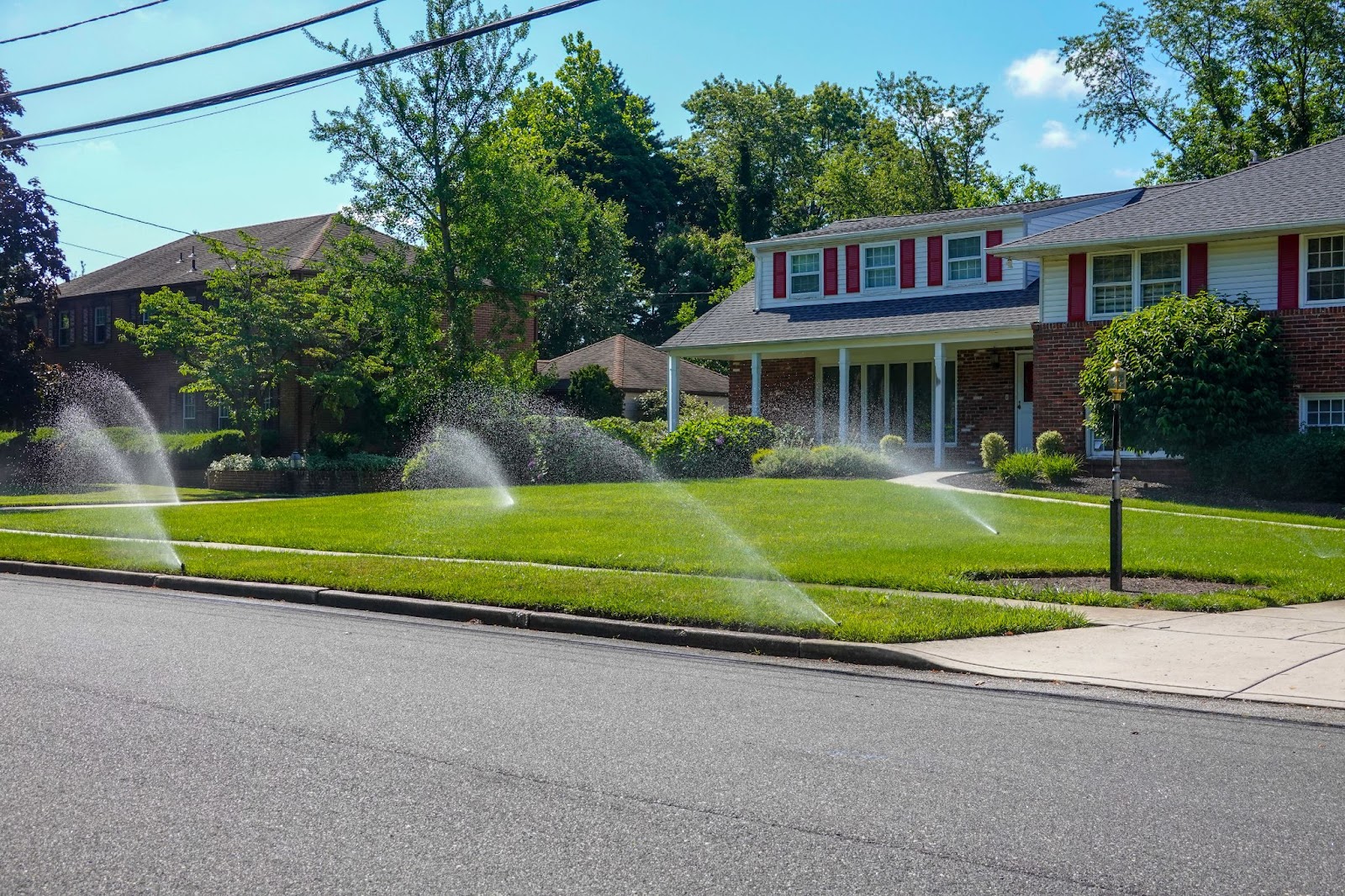 A residential neighborhood with a lawn sprinkler system watering the grass, promoting proper lawn care