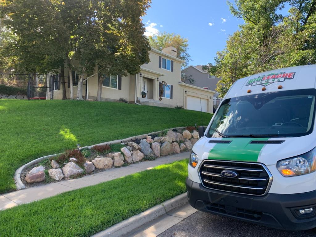 A green and white van advertising lawn care services parked in front of a house.
